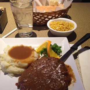 Baked steak with mashed potatoes, corn and bread.