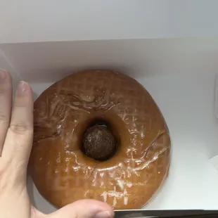 Very large glazed donut (with a chocolate donut hole in the center) hand for size.