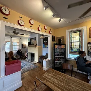 a woman sitting at a table in a room with clocks on the wall