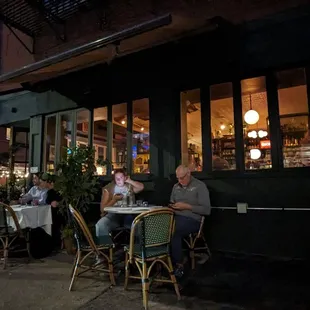 a group of people sitting outside a restaurant at night