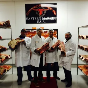 a group of men in white coats standing in front of racks of meat