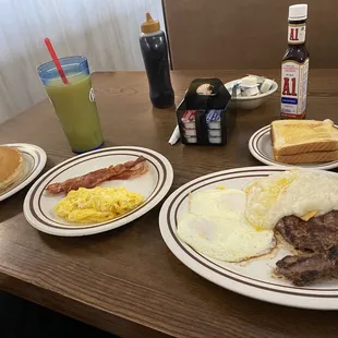 Left: pancakes, bacon, eggs. Right: steak and grits with eggs and toast. Orange juice.