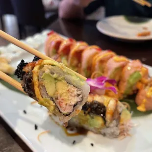 a person holding chopsticks over a plate of sushi