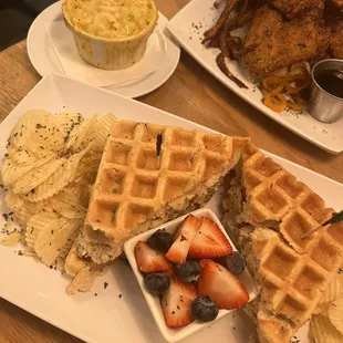 a plate of waffles, a bowl of fruit, and a plate of chips