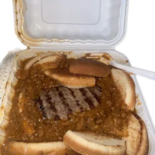 a hot dog with chili and mustard in a styrofoam container