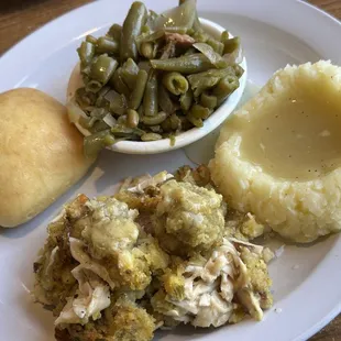 Chicken with dressing, mashed potatoes, green beans, and a roll.