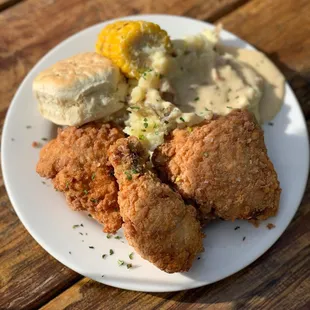 Country fried chicken with mashed potatoes, country sausage gravy, corn on the cob and biscuit.