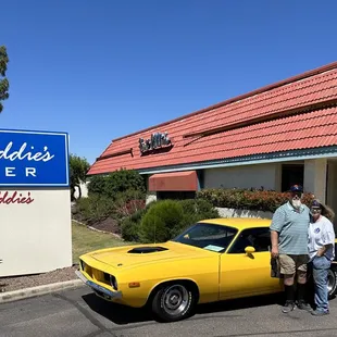 a man and woman standing in front of a yellow car