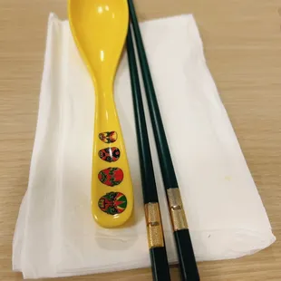 a yellow spoon and chopsticks on a napkin
