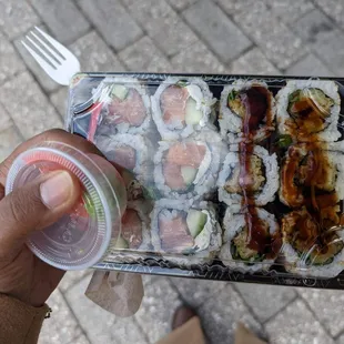 a person holding a container of sushi