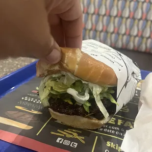 a hand grabbing a hamburger from a tray