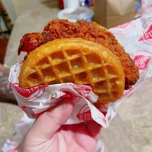 a hand holding a fried chicken and waffle sandwich
