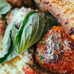 a meatball sandwich with basil leaves