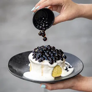 a person pouring blueberries onto a cake