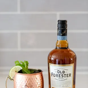a bottle of old forester next to a copper mug