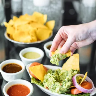 a hand dipping a tortilla into a bowl of guacamole