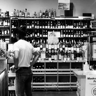 a black and white photo of a man looking at bottles of wine