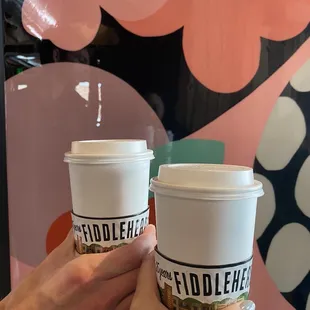 a hand holding two cups of coffee