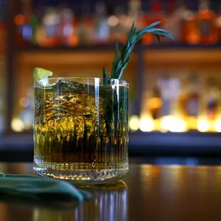 a glass of whiskey with a sprig of rosemary