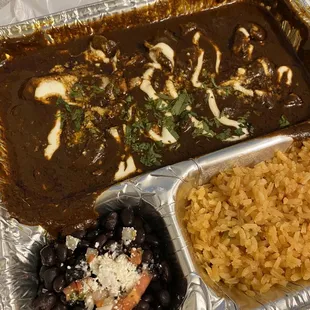 Pollo en mole with black beans and rice to go. It is delicious and I&apos;m sure it would look more appetizing on a regular plate.