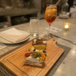 a wooden cutting board on a table with a glass of wine in the background