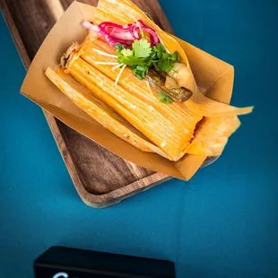 Green Chile Pork Tamales topped with cilantro, pickled red onions, roasted green chile and radish sprouts.