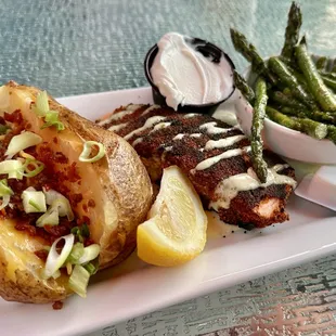 Blackened Salmon drizzled with a serrano pepper cream sauce with a loaded baked potato and vegetable of the day