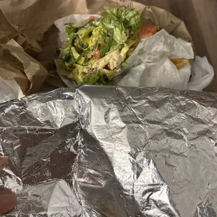 a hand holding a sandwich wrapped in foil