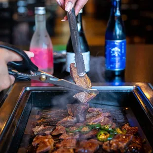 a person using tongs to grill a steak
