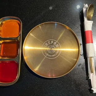 (I think) soybean paste, garlic and soy sauce, and orange chili. Small plate. Spoon, chop sticks, and straw.