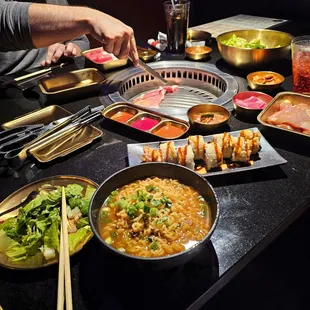 Pictured here is Ramen, tempura shrimp, variety of kimichi, salad and sauces. Cooking is steak and soy chicken.