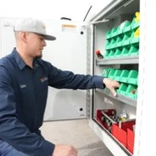 A picture of a man in front of a work truck with the side storage compartment open selecting a part