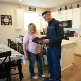 A picture of a technician standing in a customer's kitchen showing information on a tablet with a First Rate Plumbing, Heatin...