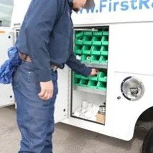 A picture of a man in front of a work truck with the side storage compartment open looking for a part