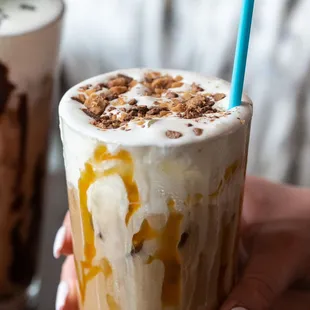 a hand holding a cup of ice cream and caramel