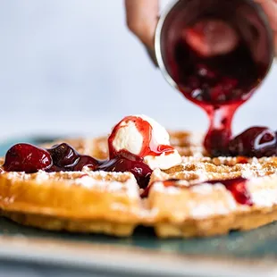 someone pouring syrup onto a waffle