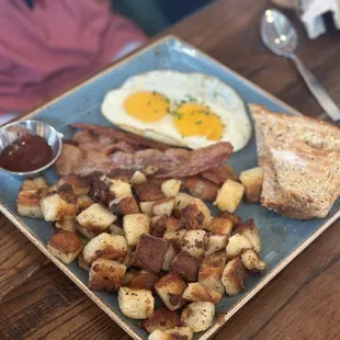 Classic breakfast - sunny side up eggs bacon flavorful hash browns and toast.