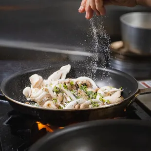 a person sprinkling salt onto a pan of food