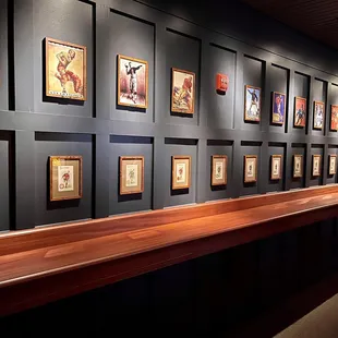 a long wooden bench in front of a wall of framed art