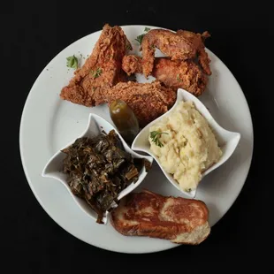 a plate of fried chicken, mashed potatoes, and greens