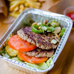 A photograph of the contents of a Five Guys burger bowl, which include two ground beef patties, tomatoes, jalapenos, lettuce ...