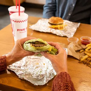 A customer&apos;s hands hold a Five Guys lettuce wrap at a dining room table inside a Five Guys restaurant.