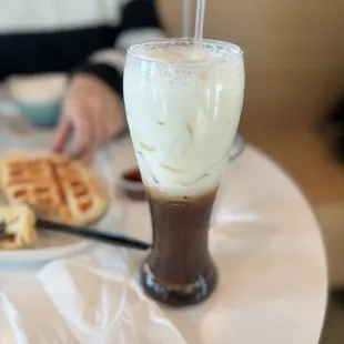 a person sitting at a table with a plate of waffles and a drink