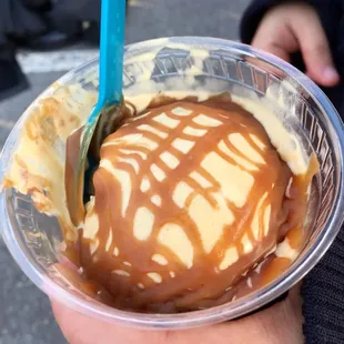 a hand holding a cup of ice cream and caramel
