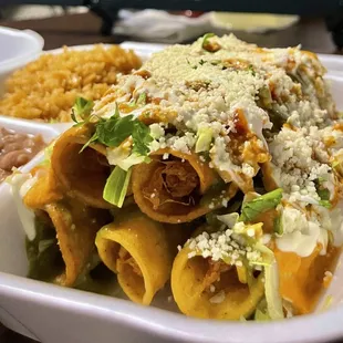 Signature Flauta combo with rice and beans. Topped with lettuce, tomato, onion, cilantro, crema, green sauce, cotija cheese and Royal sauce