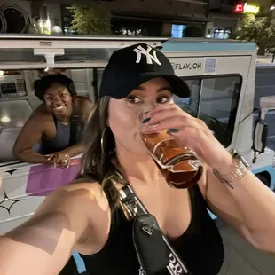 a woman drinking a beer while a man takes a selfie