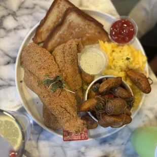 Fried fish, roasted potatoes, onions, and peppers with scrambled eggs with toast and a side of ketchup, tartar sauce, and jelly.