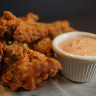 a bowl of dipping sauce next to a pile of fried chicken