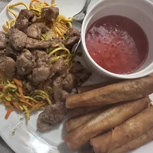 Pancit noodles topped with chicken adobo (left), a bowl of their red sauce, (bottom right) ginger chicken lumpia.