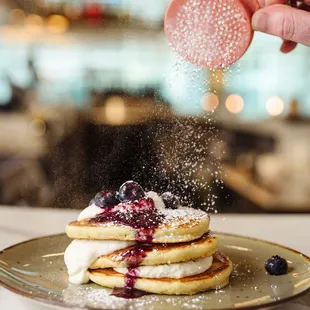 a person sprinkling sugar on a stack of pancakes